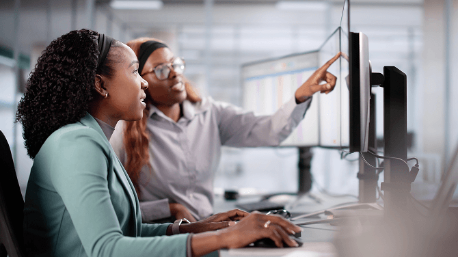 Two admins are working together in an office on a computer to enhance claim management efficiency.