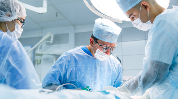 Three surgeons in scrubs and masks collaborate in a hospital operating room during a medical procedure.