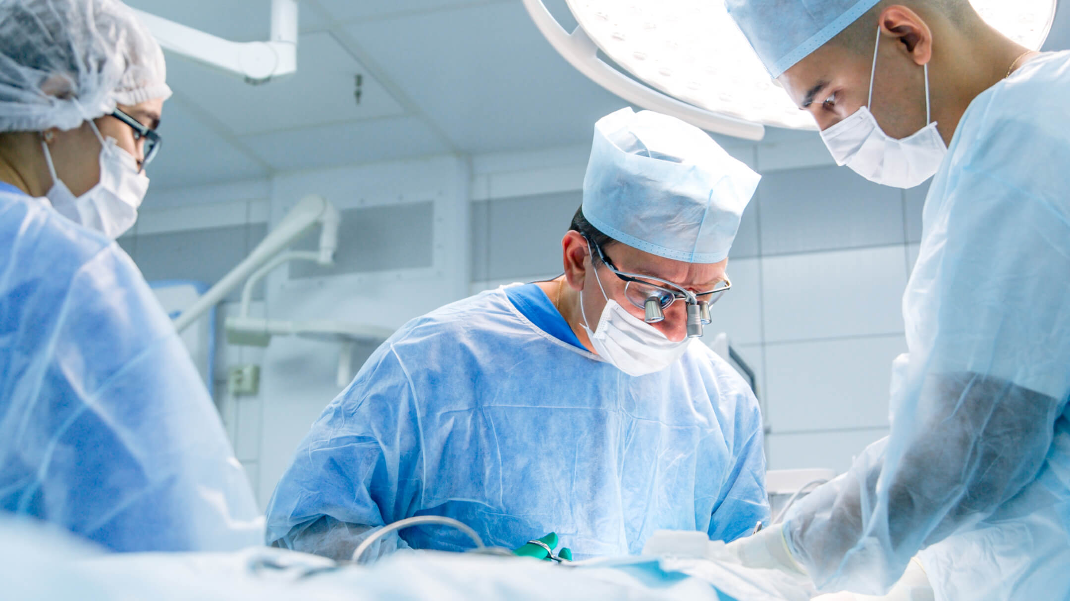 Three surgeons in scrubs and masks collaborate in a hospital operating room during a medical procedure.