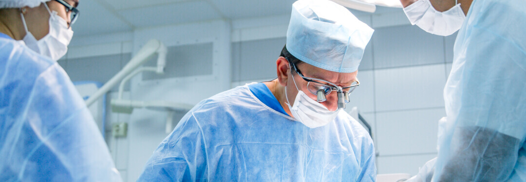 Three surgeons in scrubs and masks collaborate in a hospital operating room during a medical procedure.
