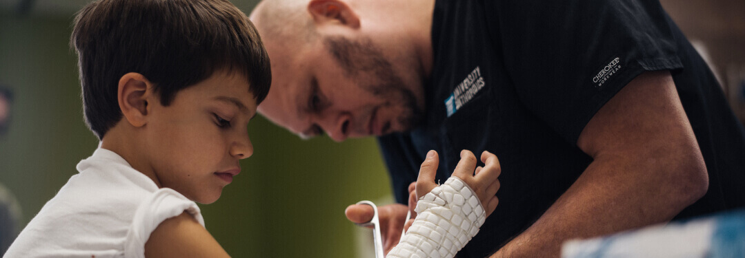 A medical professional assists a young patient by removing a cast with a pair of medical shears.