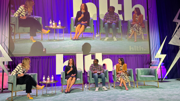 A panel of people sitting on stage discussing the theme of scaling advanced primary care through technology.