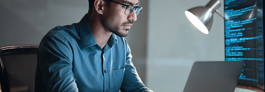 Healthcare professional sitting at a desk looking at computer screens with data.