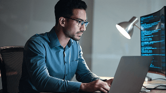 Healthcare professional sitting at a desk looking at computer screens with data.