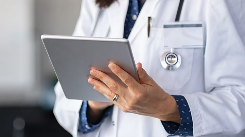 Physician with white coat and stethoscope holding a tablet to view medical records
