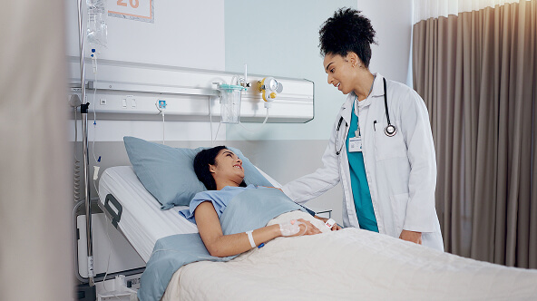 Physician standing beside a patient lying in bed at an ambulatory surgery center, illustrating the patient-centered care of ASCs.