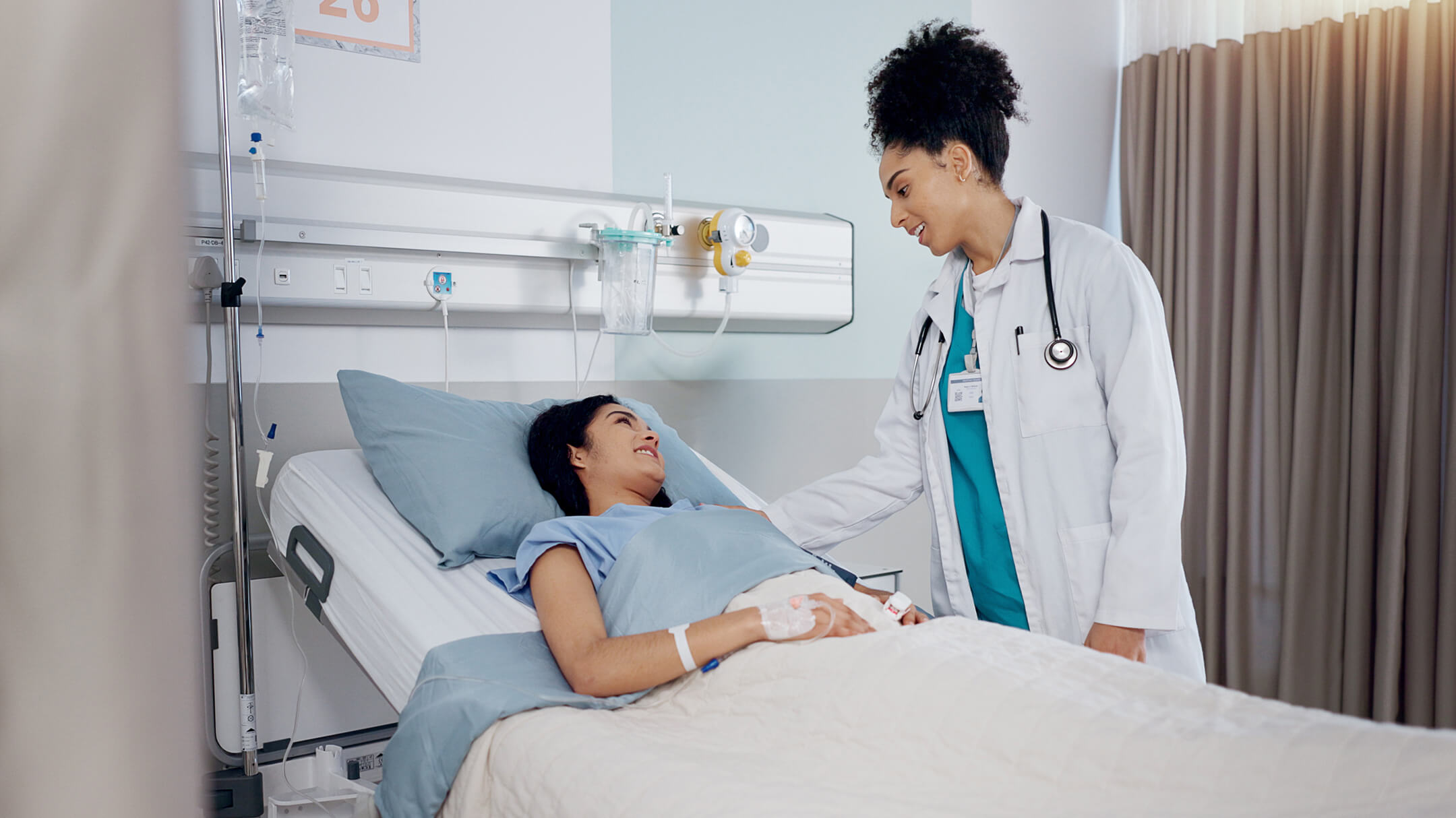 Physician standing beside a patient lying in bed at an ambulatory surgery center, illustrating the patient-centered care of ASCs.