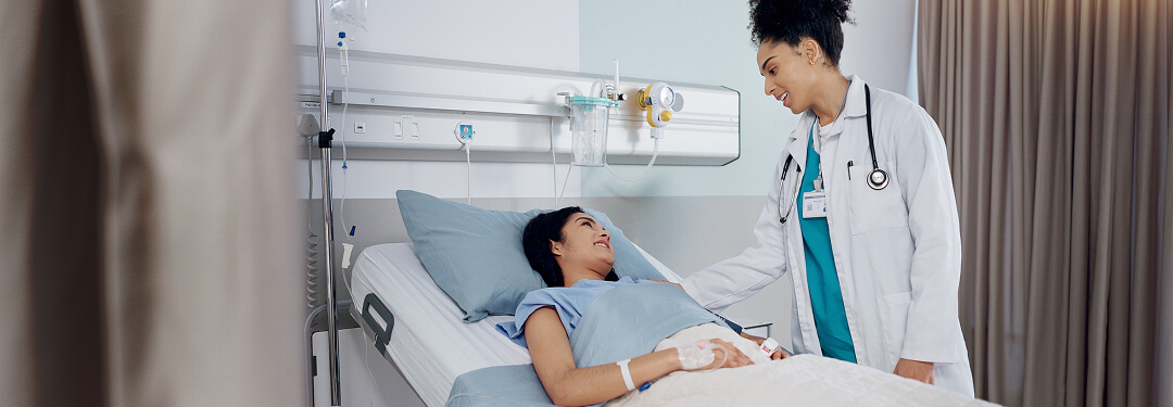 Physician standing beside a patient lying in bed at an ambulatory surgery center, illustrating the patient-centered care of ASCs.