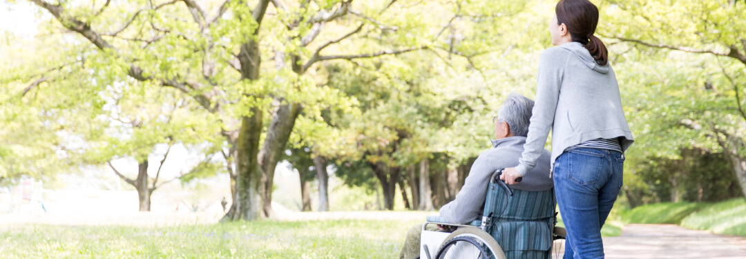 Caregiver walks patient in a wheelchair through park
