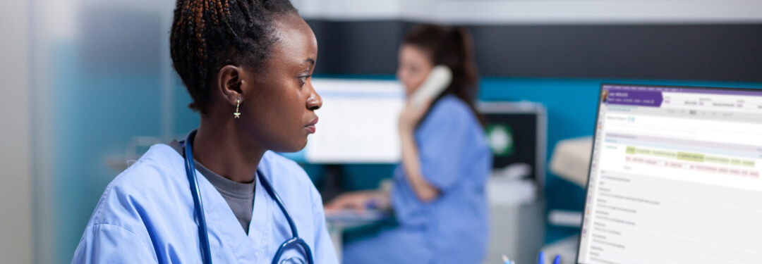 A nurse in scrubs working in EHR at the administration desk