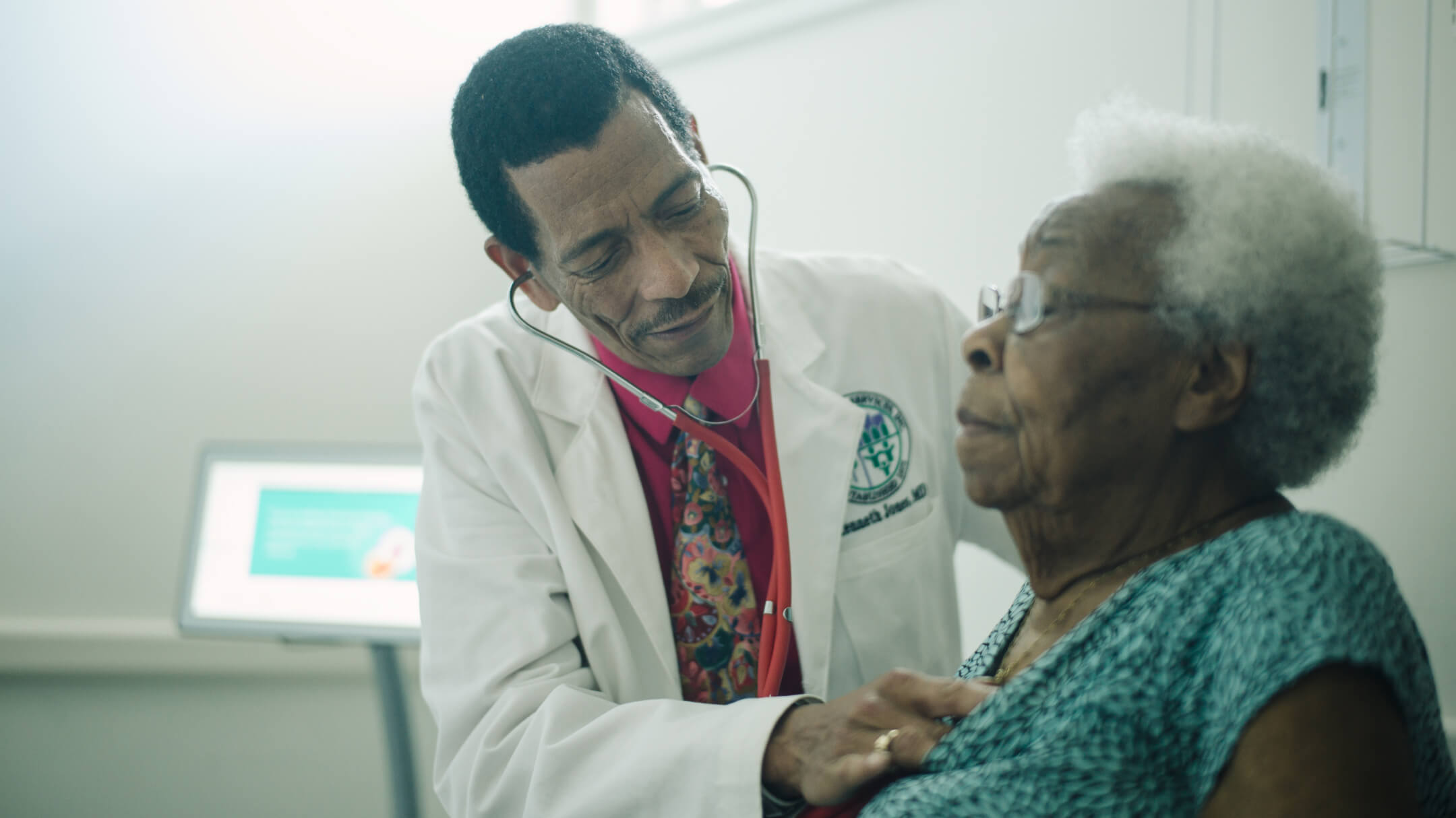 A doctor uses a stethoscope to monitor the heart rate of an elderly patient in a medical setting.