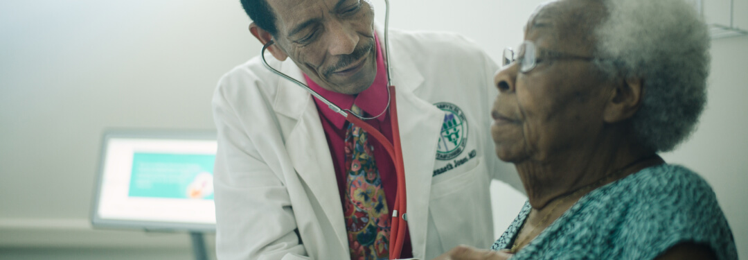 A doctor uses a stethoscope to monitor the heart rate of an elderly patient in a medical setting.
