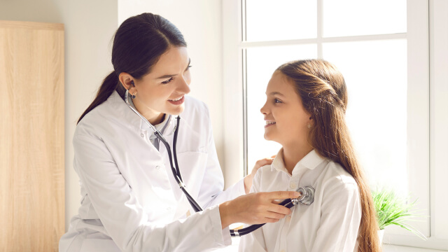 Female physician using a stethoscope to listen to a patient's heart in a concierge medicine office.