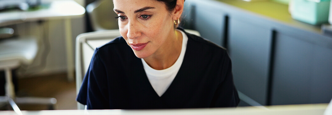 Woman in scrubs at computer.