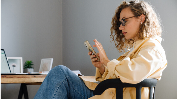 A woman sits comfortably at her desk, looking through her phone for holistic women's health apps.