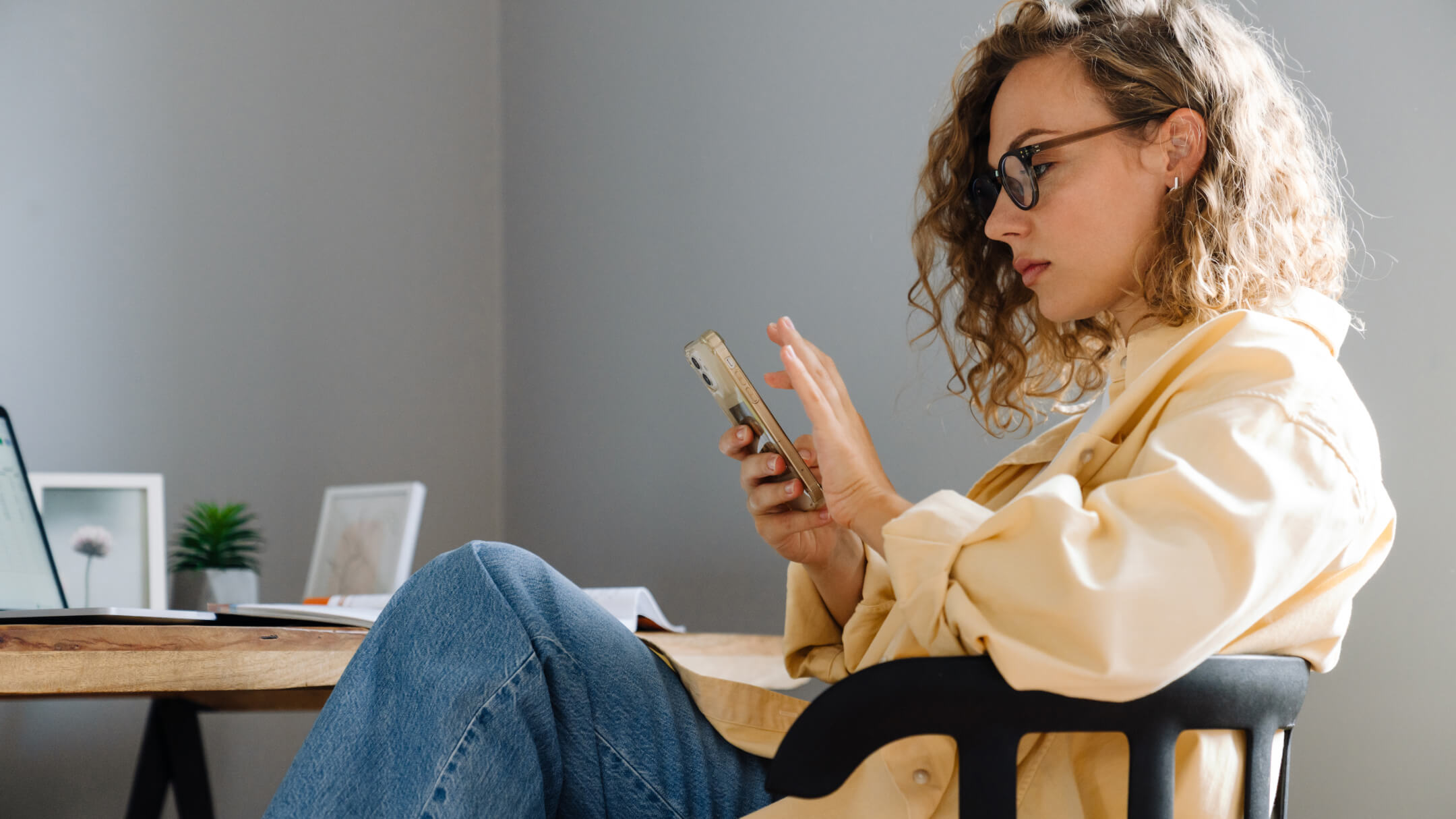 A woman sits comfortably at her desk, looking through her phone for holistic women's health apps.