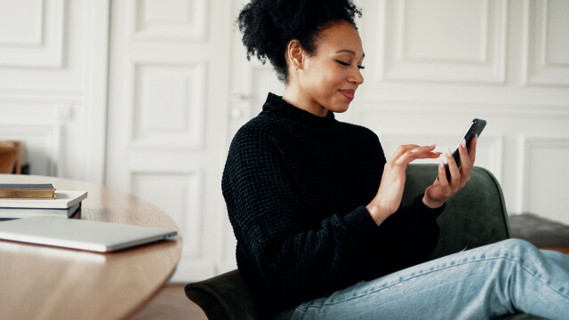 A patient sitting on a couch and using her phone represents improved patient experience with Yosi Health.