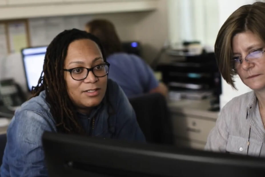An office setting with two staff working together viewing information on a monitor